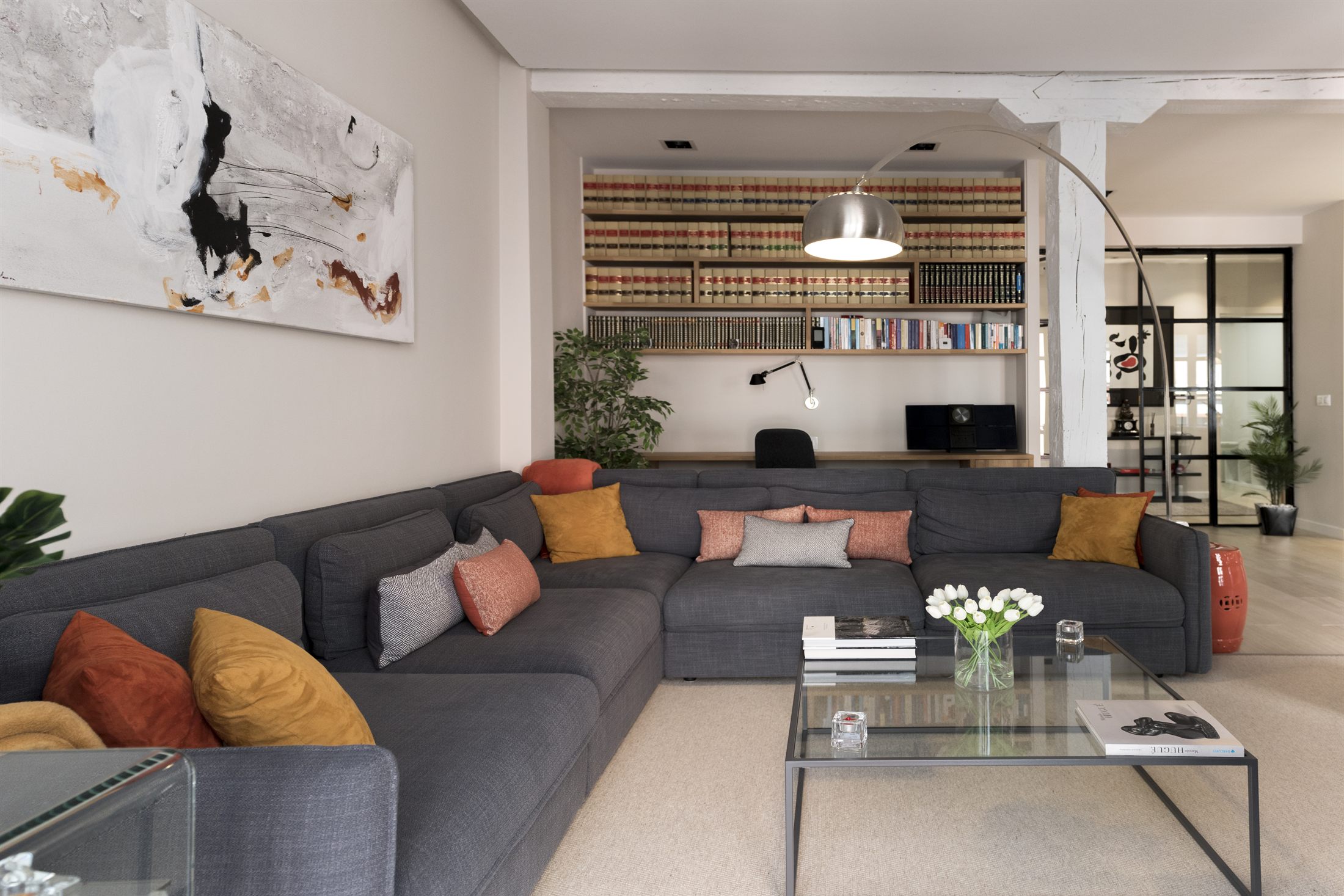 Salón de Casa Ensanche: sofá gris, cojines terracota y mostaza, estantería biblioteca a medida, lámpara de arco — proyecto real de Itek Interiorismo en Bilbao
